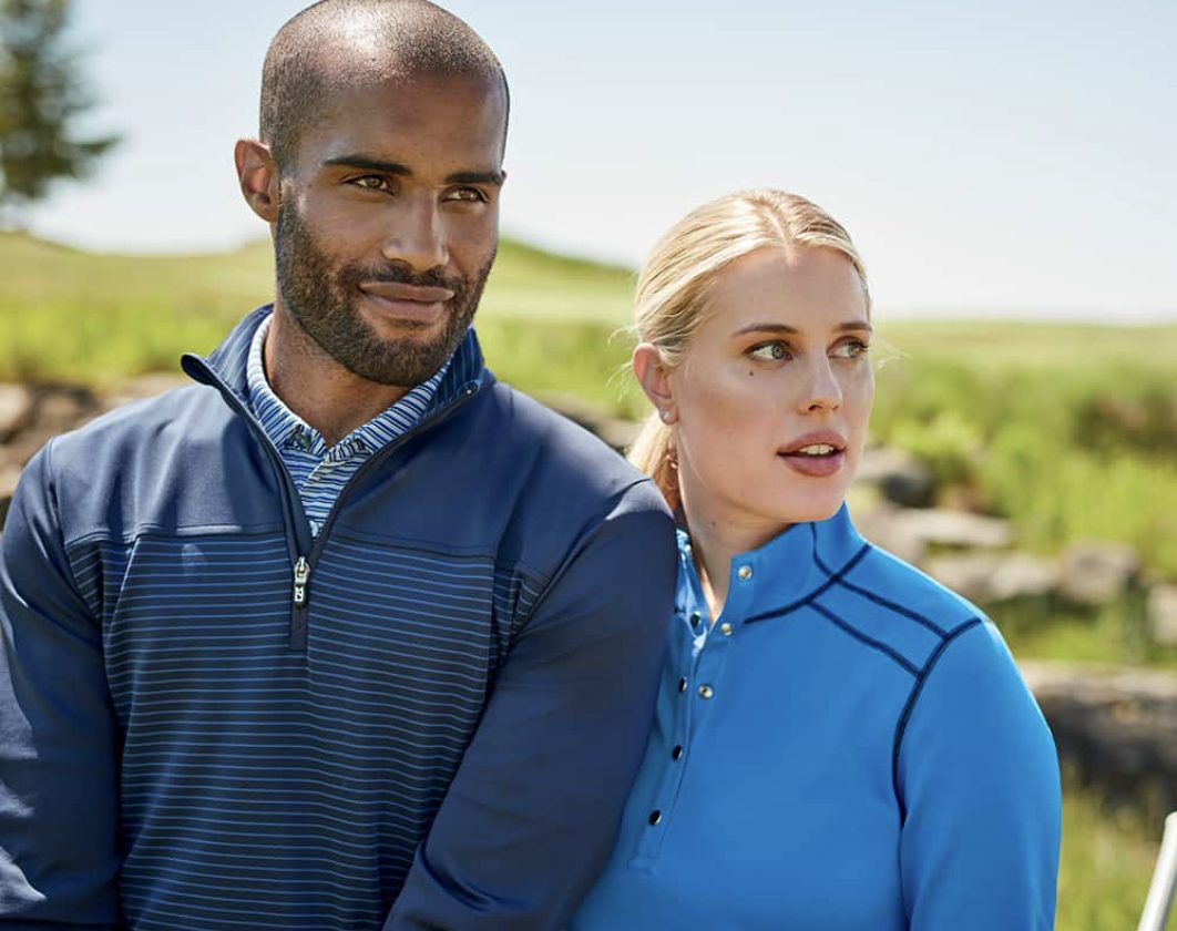 Two colleagues on a golf course in decorated navy and blue quarter-zips